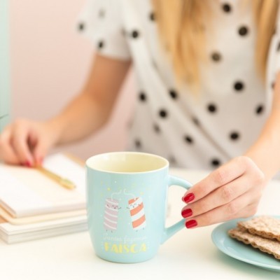 Caneca azul clara com ilustração e texto 'Vamos ficar FÁISCA' numa mesa com bolachas e livro