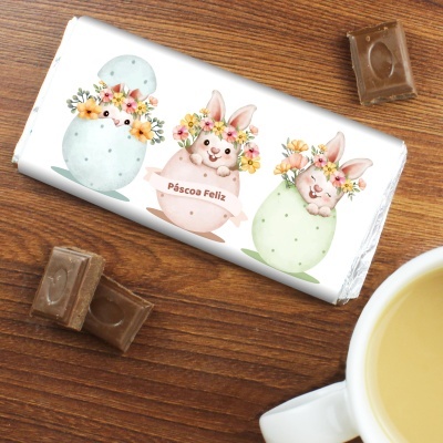 Barra de chocolate com embalagem decorada com ovos de páscoa e coelhos, mesa de madeira, pedaços de chocolate e chávena de chá