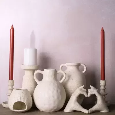 Peças decorativas em cerâmica bege com castiçais e esculturas de mãos formando coração