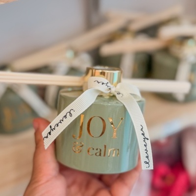 Difusor de aroma verde com texto dourado JOY & calm e laço branco com texto