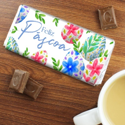 Barra de chocolate embrulhada com papel decorativo de Páscoa, pedaços de chocolate e chávena de bebida