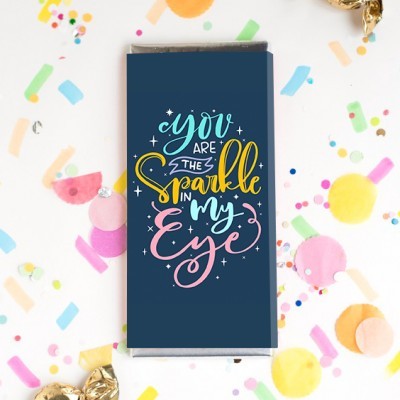 Embalagem azul de barra de chocolate com texto colorido e confetes ao redor.