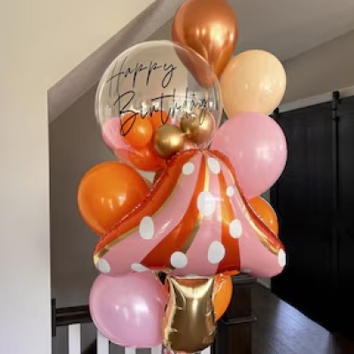 Balões coloridos para aniversário com balão claro a dizer 'Happy Birthday' e balão em forma de cogumelo rosa com bolinhas brancas