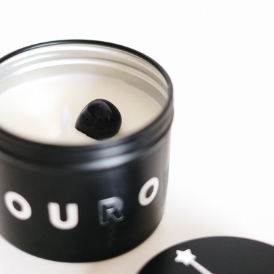 Vela preta com texto 'OURO' e tampa com constelação branca