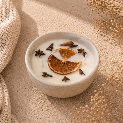 Vela artesanal branca em recipiente cinzento com decoração de laranja seca e especiarias