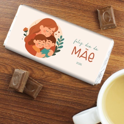 Tablete de chocolate com embalagem feliz dia da MÃE 2026 sobre mesa de madeira com chá