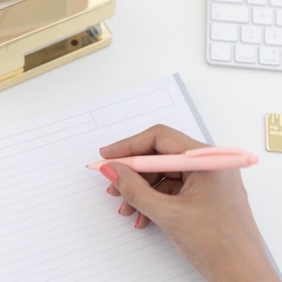 Mão escrevendo com caneta cor de rosa em papel pautado branco