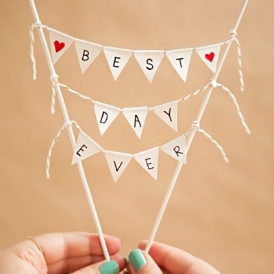 Topo de bolo com bandeirolas de papel branco e letras pretas formando BEST DAY EVER com corações vermelhos.