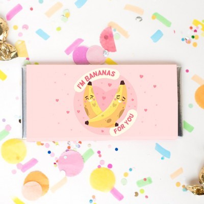 Embalagem de chocolate rosa com bananas ilustradas e texto humorístico, rodeada por confetes coloridos