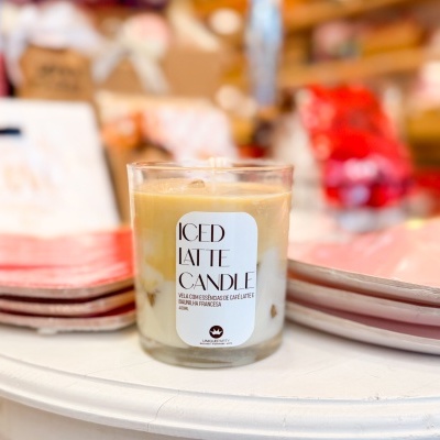Vela aromática Iced Latte Candle em copo de vidro sobre mesa branca com pratos rosa ao redor