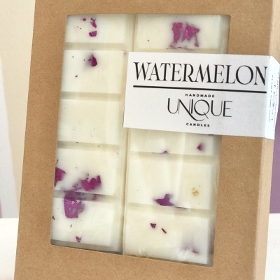 Vela branca artesanal com pedaços roxos embalada em caixa de cartão com etiqueta branca