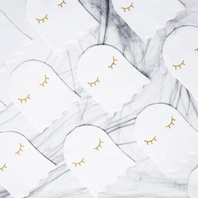 Máscaras de dormir brancas com cílios dourados desenhados, sobre superfície de mármore