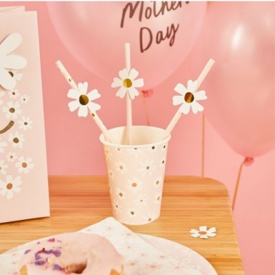 Copos e palhinhas decoradas com flores, balões cor de rosa e saco para presente sobre mesa de madeira