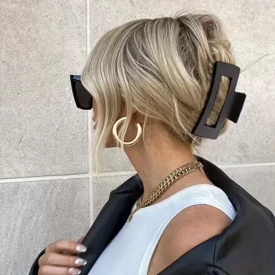 Mulher com presilha preta no cabelo e acessórios dourados contra parede cinzenta