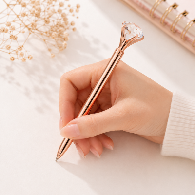 Caneta rose gold com topo de cristal sendo segurada por mão