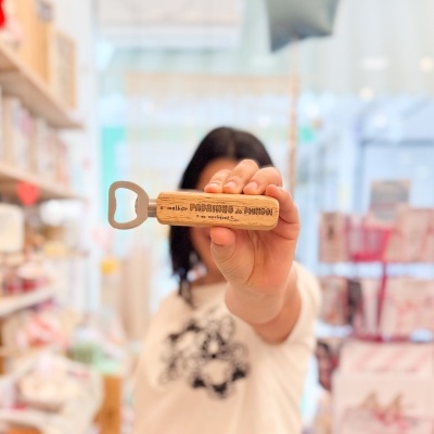 Abridor de garrafas com pega de madeira clara e texto gravado em loja