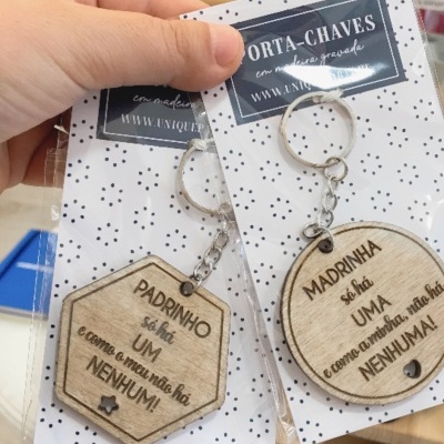 Chaveiros de madeira com mensagens gravadas para padrinho e madrinha, embalados em cartão branco com bolinhas pretas.