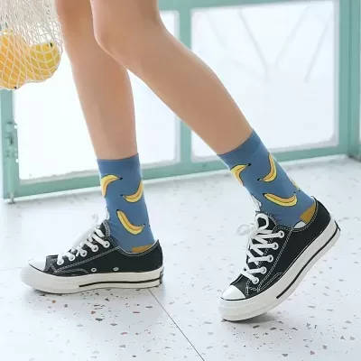 Meias azuis com bananas amarelas e ténis pretos em chão branco salpicado