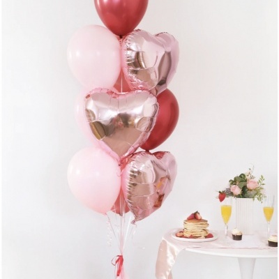 Balões rosa e vermelhos com balões metálicos em forma de coração ao lado de uma mesa com panquecas e bebidas