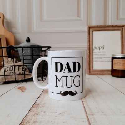 Caneca branca com texto DAD MUG e bigode em fundo de cozinha