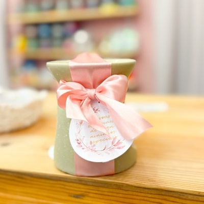 Embalagem de presente verde com laço rosa e etiqueta decorativa sobre mesa de madeira