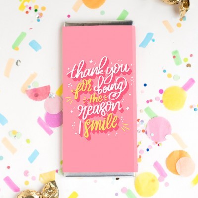 Barra de chocolate com embalagem rosa e texto manuscrito rodeada de confetes coloridos