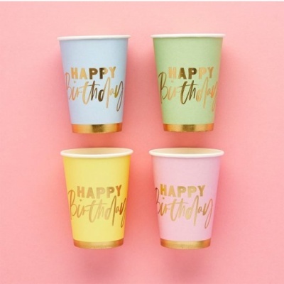 Copos de papel coloridos com texto dourado HAPPY Birthday em fundo rosa.