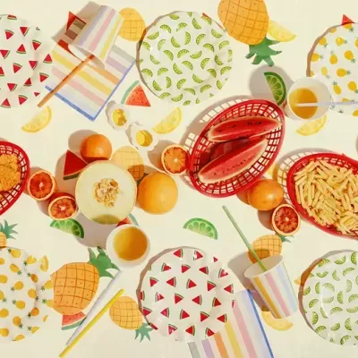 Mesa com toalha decorativa, pratos descartáveis, cestinhos com comida e copos com canudos