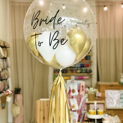 Balão transparente com texto 'Bride To Be' e balões dourados e brancos no interior