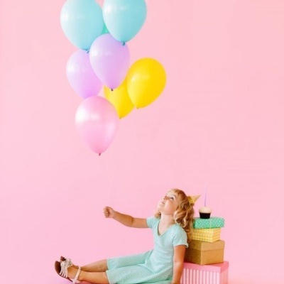 Menina sentada no chão cor de rosa com balões coloridos e caixas de presente
