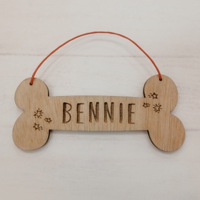 Placa de madeira em forma de osso com o nome BENNIE gravado e fio vermelho para pendurar