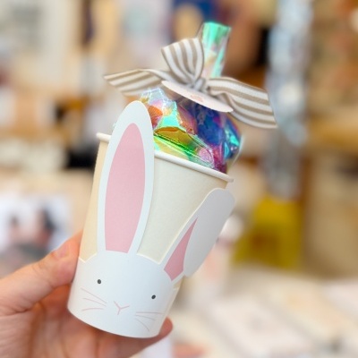 Copo de papel branco com decoração de coelho e saco de presente holográfico.