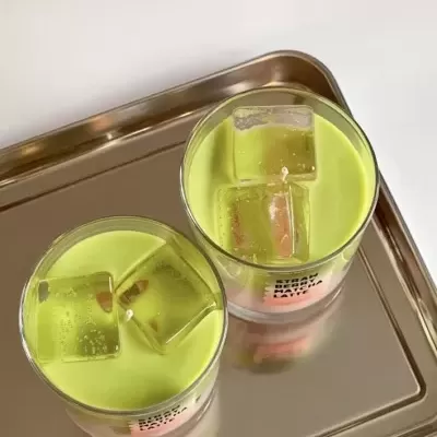 Dois copos com vela verde e gelo decorativos numa bandeja metálica