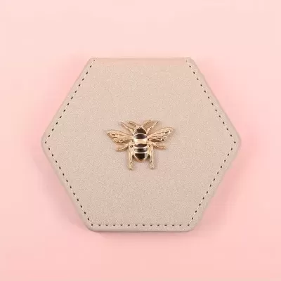 Estojo hexagonal bege com abelha dourada no centro