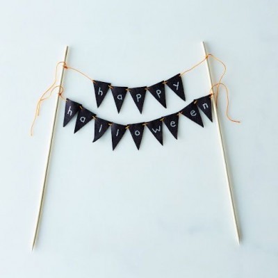 Decoração de festa com bandeiras pretas e letras brancas a dizer 'happy halloween' suspensas em fios laranja entre paus de madeira