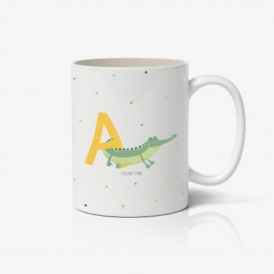 Caneca branca com letra A amarela e desenho de crocodilo verde.
