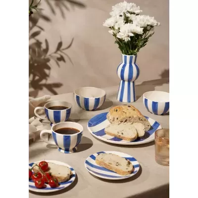 Louça decorada com riscas azuis e brancas com pão e flores numa mesa