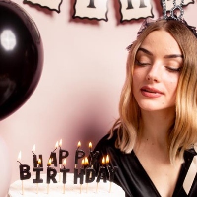 Bolo de aniversário com velas HAPPY BIRTHDAY, mulher com vestido preto e tiara 18, balão preto e bandeirola decorativa
