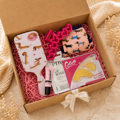 caixa de presente com produtos de beleza e acessórios em tons de rosa, incluindo escova de cabelo, meias e máscaras