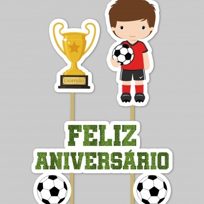 Decoração de bolo com troféu, menino com bola, bolas de futebol e texto FELIZ ANIVERSÁRIO.