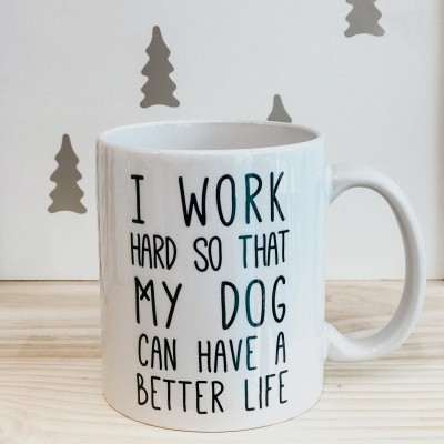 Caneca branca com texto em preto sobre uma mesa de madeira clara e fundo branco com formas de árvores