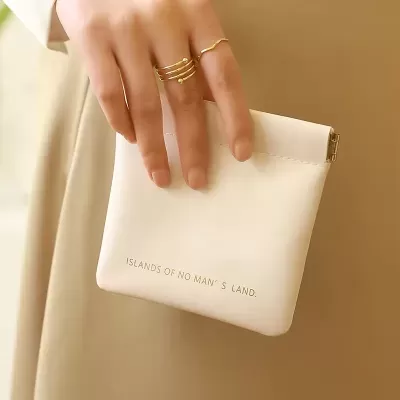bolsa pequena creme com texto e mão com anéis dourados