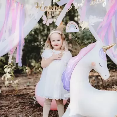 Criança numa festa ao ar livre com decoração de unicórnio e balões coloridos