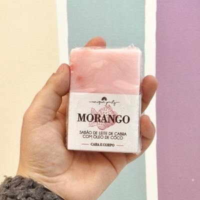 Sabão rosa Morango com etiqueta branca segurado em mão, fundo listrado colorido