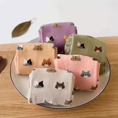 Saquinhos de tecido coloridos com padrões de gatos sobre prato branco numa mesa de madeira