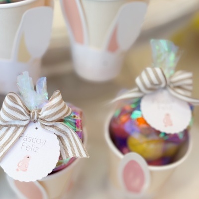 Copos decorados com orelhas de coelho e sacos de doces com laço e etiqueta de Páscoa