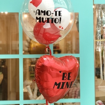 Dois balões, um transparente com texto AMO-TE MUITO! e outro vermelho coração com texto BE MINE