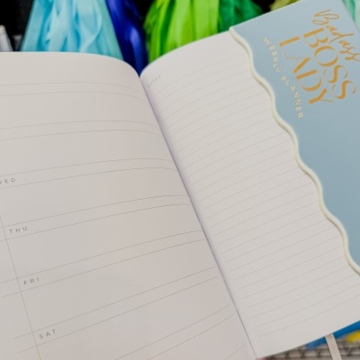 Planner semanal aberto com capa azul claro e texto dourado BOSS LADY