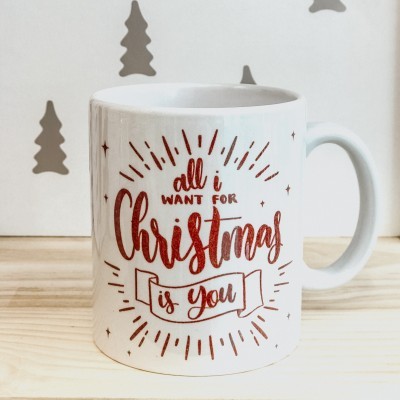 Caneca branca com texto vermelho brilhante 'all i WANT FOR Christmas is you' em fundo branco com decoração natalícia