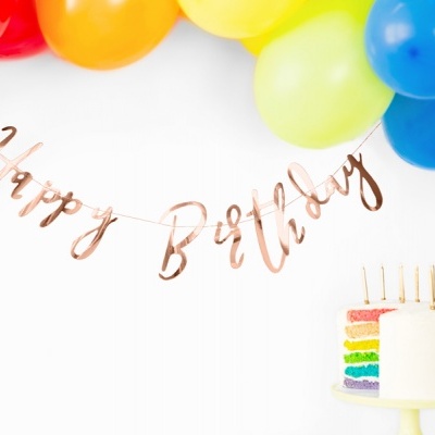 Decoração de aniversário com balões coloridos, faixa 'Happy Birthday' dourada e bolo em camadas coloridas